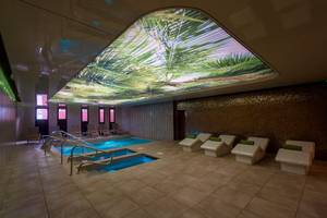 Innenpool im HD Parque Cristobal mit Palmenprojektion an der Decke und Liegen.