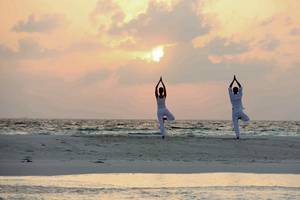Zwei Personen machen Yoga am Strand bei Sonnenuntergang am Baros Maldives Resort.