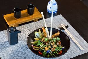 Ein Salat in einem schwarzen Teller mit Besteck auf dem Tisch, umgeben von Utensilien.