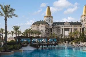 Außenansicht des Delphin Diva Premiere Hotels mit Swimmingpool, Brücke und Sonnenliegen.