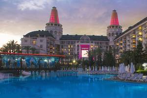 Das Delphin Diva Premiere Hotel mit beleuchteten Türmen und Swimmingpool im Abendlicht.