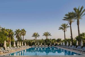 Außenpool des Delphin Diva Premiere Hotels mit weißen Sonnenliegen und Sonnenschirmen.