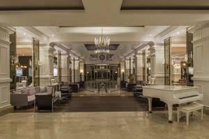 Das elegante Foyer des Delphin Diva Premiere Hotels mit einem weißen Klavier, Sofas und Kronleuchtern.