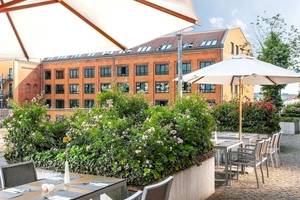 Außenbereich des NH Berlin Alexanderplatz Hotels mit Tischen und Stühlen unter Schirmen.