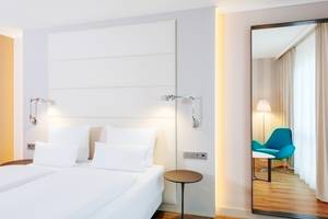 Ein modernes Hotelzimmer im NH Berlin Alexanderplatz mit zwei Betten, weißen Kissen und Nachttischen.