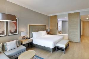 Inneneinrichtung der Suite im Hilton Cabo Verde Sal Resort mit einem großen Bett, Couch und Nachttisch.