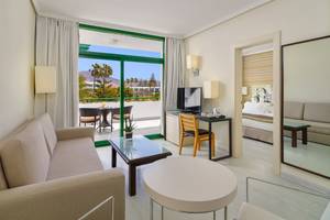 Innenansicht einer Suite im H10 Lanzarote Princess Hotel mit Wohnzimmer, Esstisch, Fernseher und Schlafzimmer.