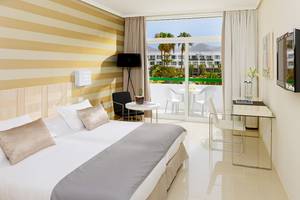 Innenansicht eines Zimmers im H10 Lanzarote Princess Hotel mit Bett, Schreibtisch und Balkon.