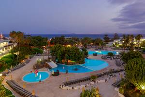 Abendausblick auf den Swimmingpool des H10 Lanzarote Princess Hotels mit Sonnenliegen und tropischen Pflanzen.