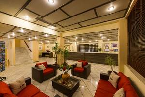 Lobby des Pavlina Beach Hotels mit roten Sofas, Tischen, Pflanzen und einer Rezeption.