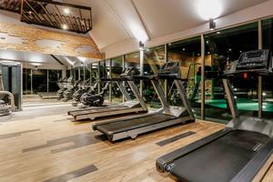 Fitness-Center im Kalima Resort & Villas Khao Lak mit mehreren Laufbändern und einem Pool im Hintergrund.
