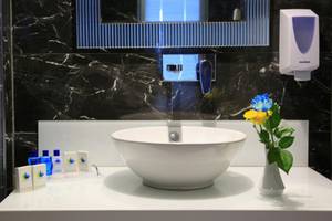 Ein Badezimmer im LABRANDA Ephesus Princess Hotel mit schwarzen Marmorfliesen, einem weißen Waschbecken und blauen Blumen in einer Vase.