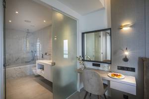 Badezimmer des Cavo Maris Beach Hotels mit Glastür, Badewanne und Schreibtisch.