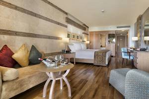 Luxuriöses Zimmer im Kempinski Hotel The Dome Belek mit Doppelbett, Schreibtisch, Sofa und Tisch mit Weinflasche und Gläsern.