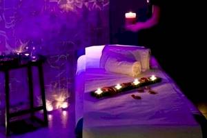 Spa-Behandlungsraum im Barcelo Raval Hotel mit violettem Licht und Kerzen auf einem Tisch.