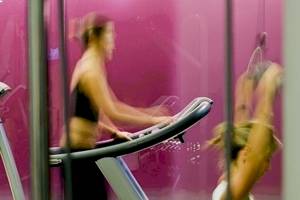 Frau auf dem Laufband im Fitnessstudio mit pinker Wand im Hintergrund