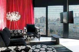 Wohnzimmer im Barcelo Raval Hotel mit schwarzem und weißem Sofa, roter Vorhang, Tisch, Fernseher und Lampen.