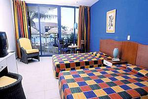 Doppelzimmer im Muthu Playa Varadero Hotel mit zwei farbenfrohen Betten, gelbem Stuhl und Fernseher.