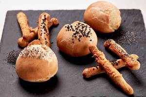 Mehrere gebackene Semmelknödel und Brötchen auf einem schwarzen Teller.