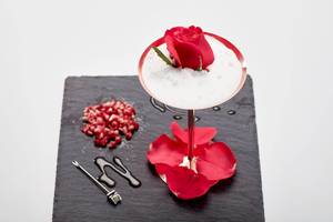 Cocktail auf schwarzem Untergrund mit roter Rose und Granatapfelsamen.
