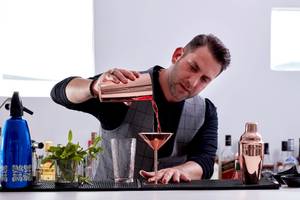 Ein Mann, der ein Glas mit einer silbernen Cocktailmischung füllt, steht an einer Bar.