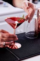 Barkeeper gibt einen Cocktail mit Thymian einhändig in ein Glas.