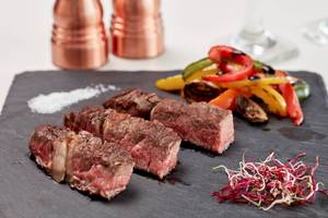 Ein Gericht mit geschnittenem Steak, gewürztem Gemüse und Salz auf einem schwarzen Teller.