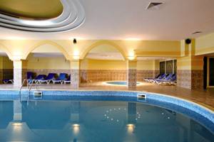 Innenpool im Festa Panorama Hotel mit blauen Liegestühlen und einer kleinen Whirlpool-Badewanne.