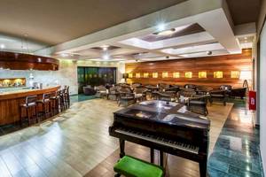 Innenbereich des Hotels Catalonia Royal Bavaro mit Bar, Klavier und runden Tischen.