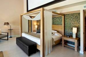 Hotelzimmer im Catalonia Royal Bavaro mit Himmelbett, Fernseher, Lampe und Nachttisch.