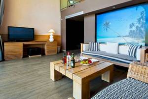 Innenraum des Catalonia Royal Bavaro Hotel mit Wohnzimmermöbeln, Fernseher, Tisch mit Flaschen und Obst.