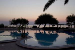 Abendstimmung am Pool im Baia del Sole Hotel mit reflektierten Bäumen und dem Meer im Hintergrund.