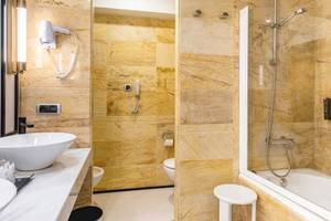 Badezimmer im Sarena de Muro Resort Mallorca mit Marmorwänden, Badewanne, Toilette und Föhn.
