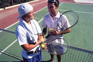 Zwei Männer stehen auf einem Tennisplatz im Calypso Beach Hotel, beide halten Tennisschläger und Tennisbälle.