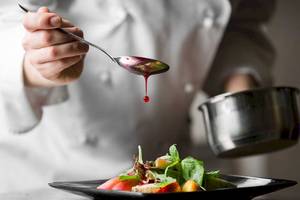 Koch tropft rote Sauce auf ein Salatgericht auf einem schwarzen Teller
