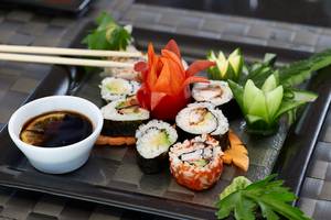 Ein Teller mit verschiedenen Sushi-Rollen, Sojasauce und Deko-Gemüse.