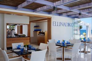 Innenansicht des Ellinadiko Restaurants mit weißen Stühlen und Tischen, Blick auf die Küche und das Meer.