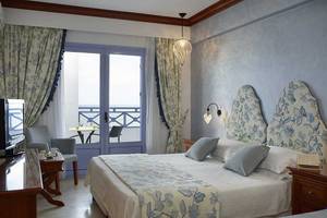 Innenansicht eines luxuriösen Hotelzimmers im Serita Beach Hotel mit einem Doppelbett, Fernseher und Balkon.