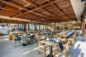 Innenansicht des Restaurants im Stella Village Hotel mit Holzmöbeln und einer offenen Küche.