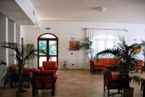 Hotellobby von Gabbiano Beach Vieste mit roten Sesseln, Pflanzen und einer Couch.