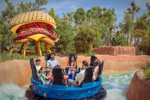 Familie im Ja Lake View Hotel auf einer blauen Wasserrutsche, mit einem riesigen Hamburger im Hintergrund.