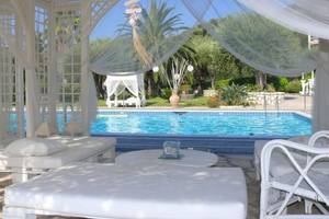 Pool-Loungebereich im Nefeli Hotel mit weißen Möbeln und Vorhängen.