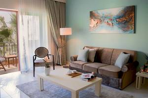 Wohnzimmer im Kempinski Hotel San Lawrenz mit Sofa, Tisch, Gemälde und Balkonaussicht.
