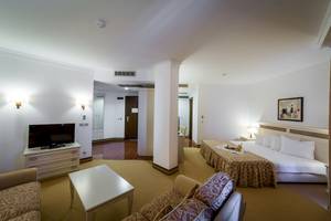 Innenansicht eines Zimmers im Helena Sands Hotel mit Fernseher, Sofa und Bett.