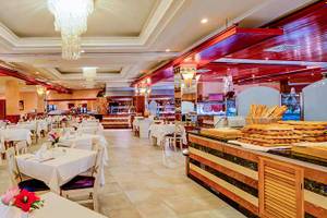 Innenansicht des Restaurants im SBH Costa Calma Beach Resort mit vielen Tischen und Stühlen, gedeckten Tischen, und einer Theke mit Brot und Backwaren.