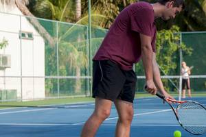 Tennisspieler in einem roten T-Shirt schlägt einen Ball auf einem blauen Tennisplatz.
