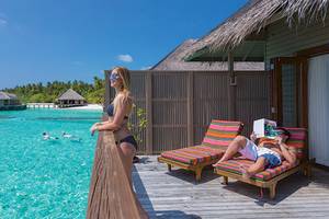 Zwei Personen entspannen auf der Terrasse des Meeru Island Resorts & Spa mit Blick auf das Meer.