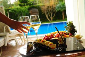 Ein Glas Weißwein und ein Teller mit buntem Obst liegt am Pool des Delphin BE Grand Resort.