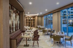 Innenansicht des Grape Kiss Restaurants im Delphin BE Grand Resort mit Tisch und Stühlen, Wandmalerei und großen Fenstern.