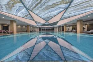 Innenansicht des Delphin BE Grand Resort mit einem modernen Pool und beeindruckender Deckenbeleuchtung.
